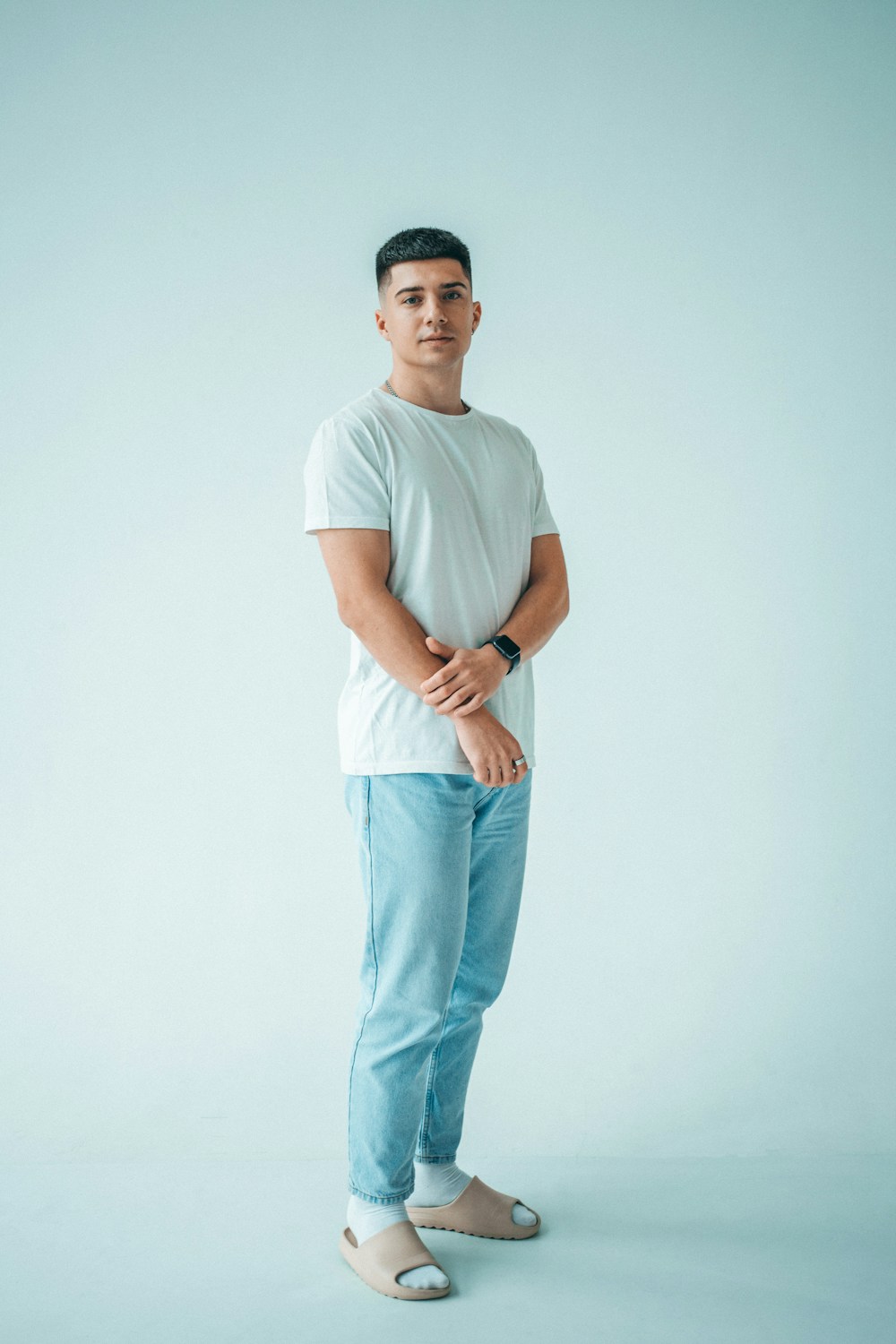 A full-length shot: head to feet, plain clothes, natural stance, plain studio backdrop